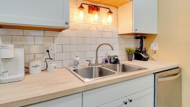 A modern kitchen with white cabinets, a double sink, a coffee maker, and a coffee and tea dispenser. - Chic Indianapolis Home w/ Yard Near Downtown! (Indianapolis)