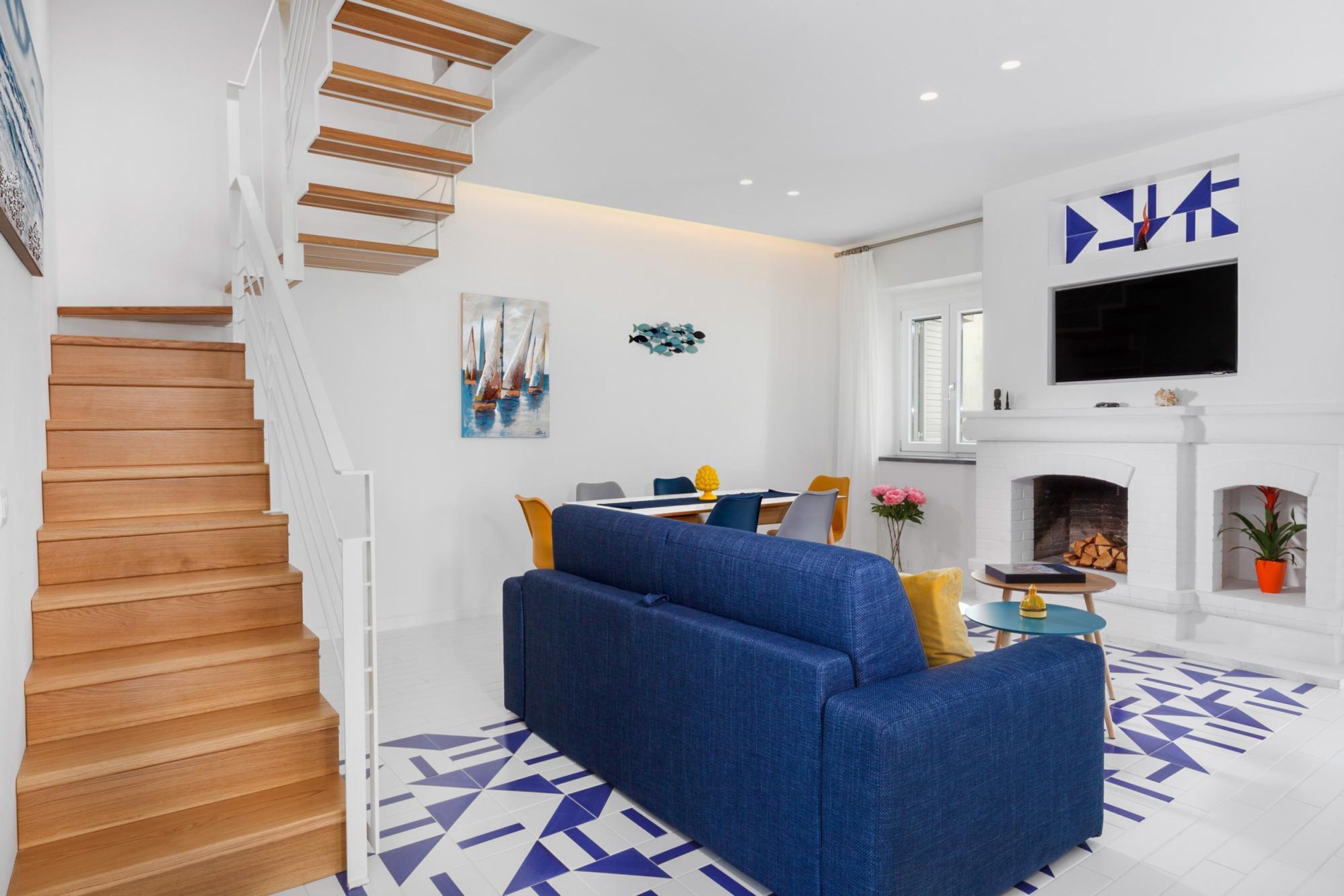 Ein modernes Wohnzimmer mit Treppe, einem blauen Sofa, einem Kamin und einem an der Wand befestigten Fernseher.