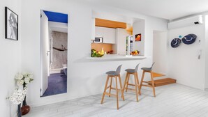 A modern kitchen with white cabinets, a microwave, and a fruit bowl. There are two wooden stools and a small table. - Leucosia in Sorrento (Sorrento)