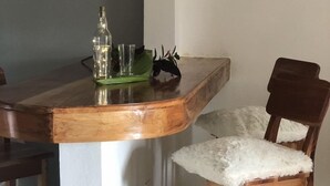 A wooden bar counter with a bottle and glasses, a white fluffy chair, and a wooden chair. - Seacret Studios - Cozy Jamaican Retreat Apts by RedAwning (Negril)