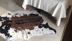 A bedroom with a bed, a wooden chair, a small table with a plant, and a cowhide rug. - Seacret Studios - Cozy Jamaican Retreat Apts by RedAwning (Negril)