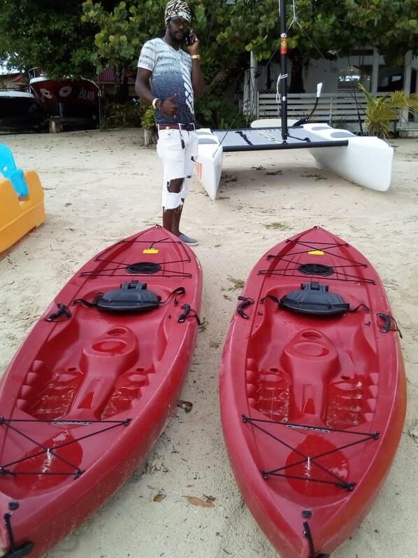 Dos kayaks rojos en una playa arenosa con una persona de pie cerca.