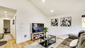 A modern living room with a flat-screen TV, a glass coffee table, a brown sofa, and abstract wall art. - Modern Pacific Vacation Rental: 5 Mi to Lake Tapps (Pacific)