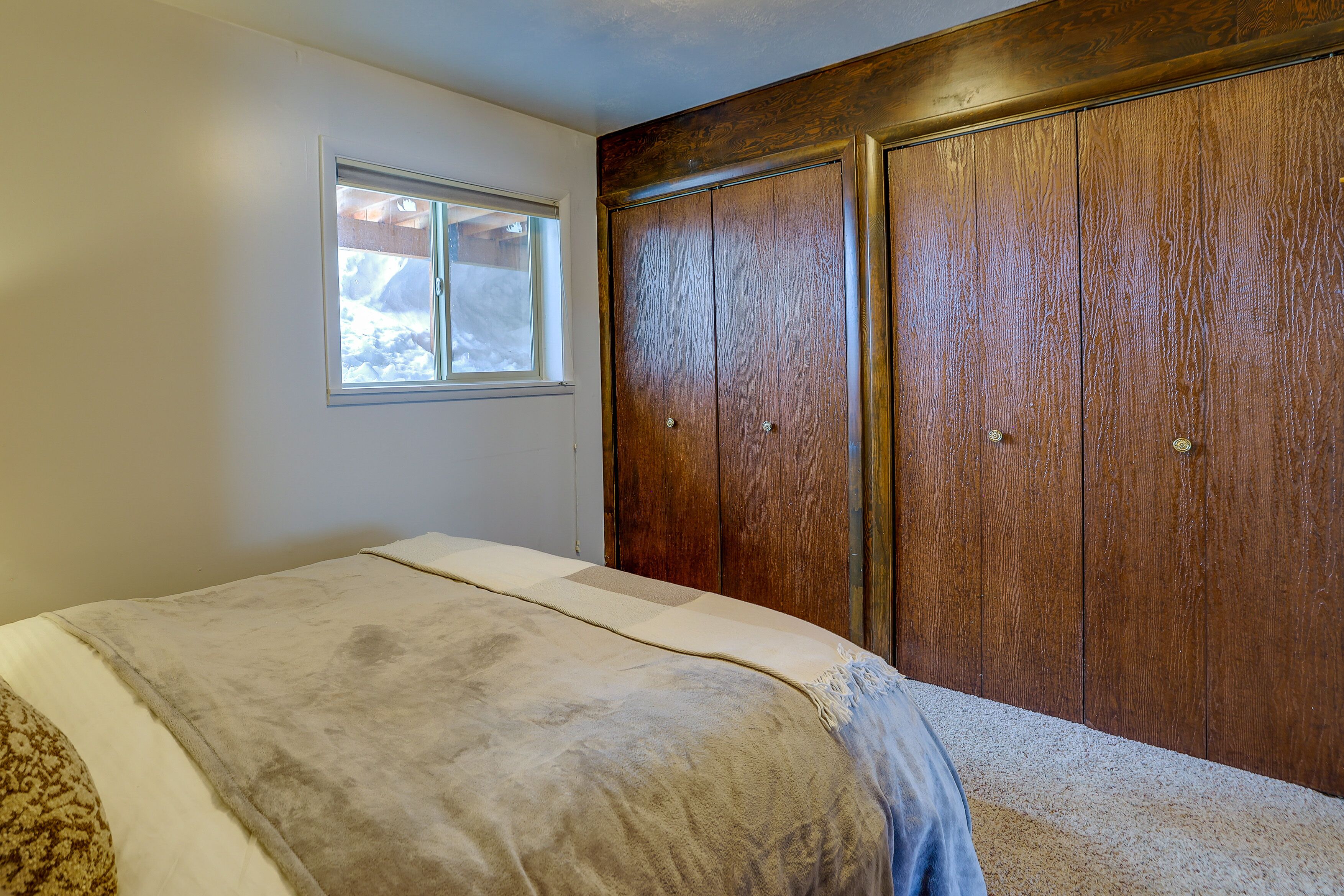 Een slaapkamer met een bed, een raam en houten kasten.
