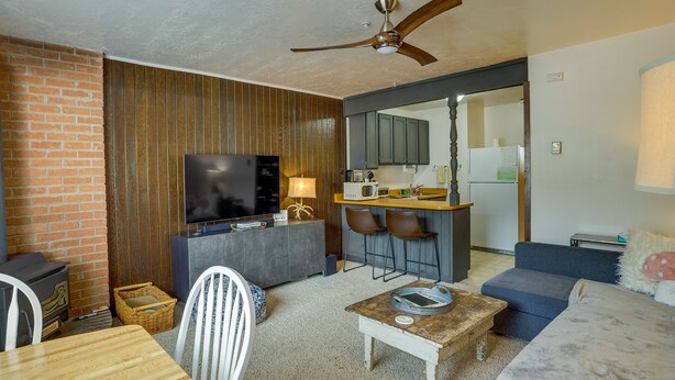 A modern living room with a TV, wooden furniture, a dining table, and a kitchen area in the background. - Brian Head Vacation Rental w/ On-site Ski Lift! (Brian Head)