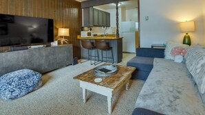 A living room with a television, sofa, coffee table, and a kitchen area in the background. - Brian Head Vacation Rental w/ On-site Ski Lift! (Brian Head)