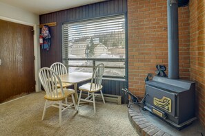 A cozy room with a brick fireplace, a window with blinds, a table with chairs, and a fire extinguisher on the wall. - Brian Head Vacation Rental w/ On-site Ski Lift! (Brian Head)