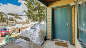 A building with a green door and windows, a snow-covered ground, and a view of a snowy mountain. - Brian Head Vacation Rental w/ On-site Ski Lift! (Brian Head)