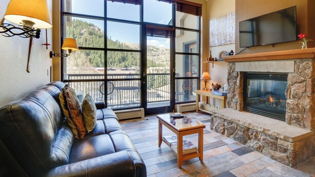 A living room with a leather sofa, a stone fireplace, and a large window offering a mountain view. - Cozy Avon Condo Near Beaver Creek Resort! (Avon)