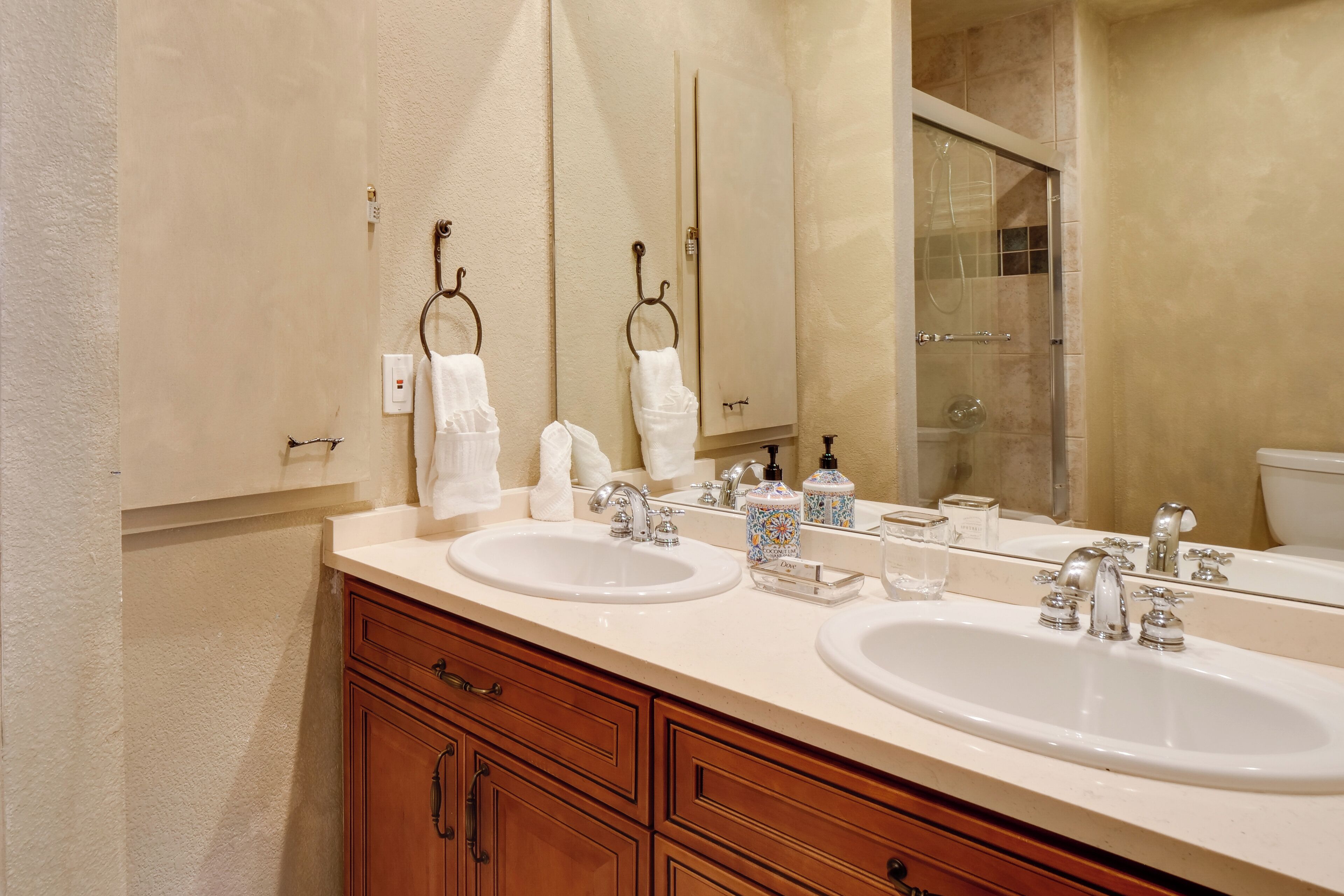 A bathroom with two sinks, wooden cabinets, a large mirror, and a shower area.