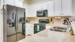 A kitchen with white cabinets, stainless steel appliances, a granite countertop, and a double sink.