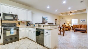 A kitchen with white cabinets, a dishwasher, and a stove. There is a dining area with a table and chairs.