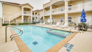 A pool area with a 5 ft no diving sign, white lounge chairs, and a blue umbrella.