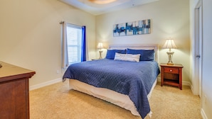 A bedroom with a large bed, two bedside tables with lamps, a ceiling fan, and a window with blinds.