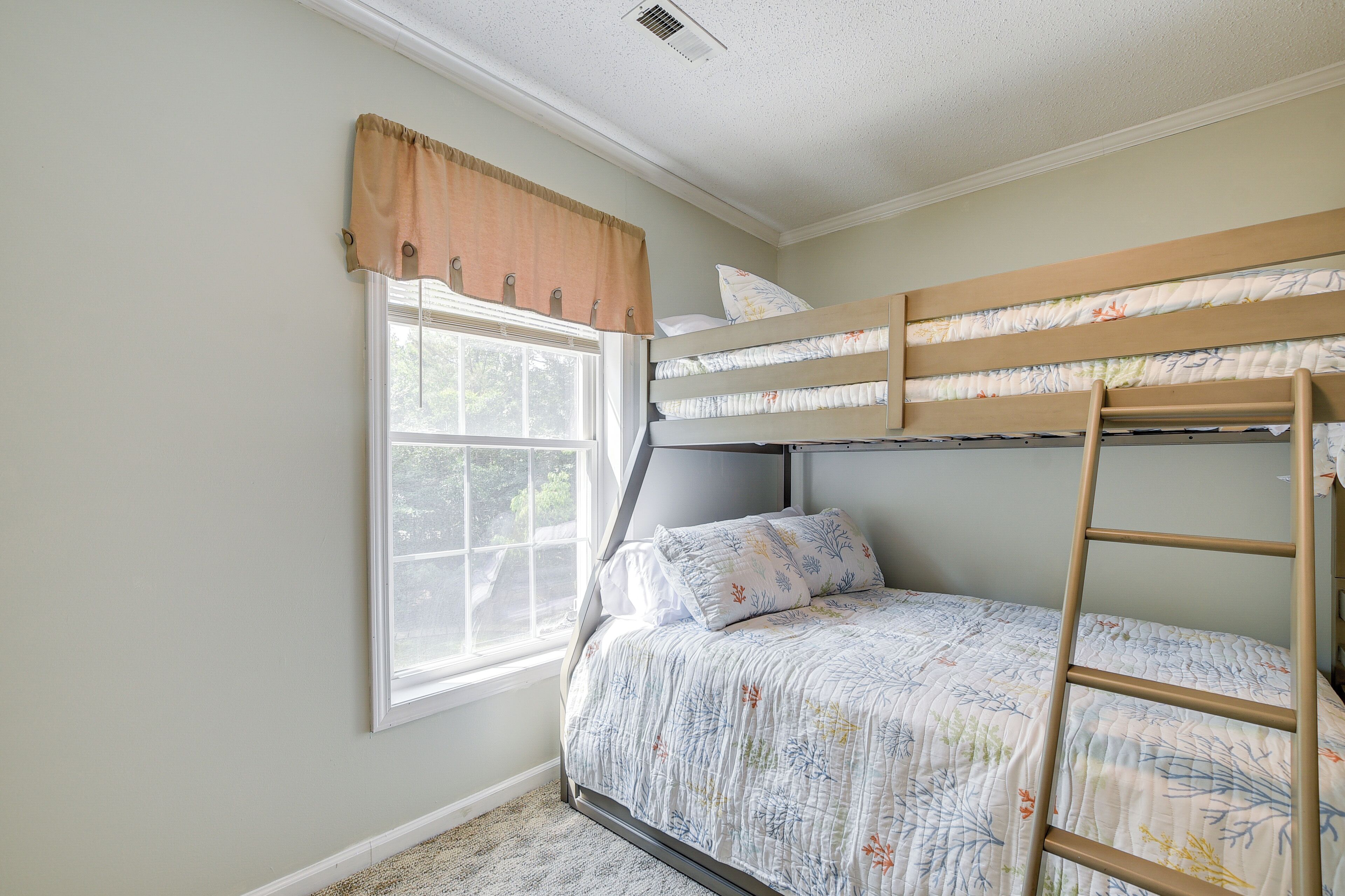 Une chambre avec un lit superposé, une fenêtre, une échelle et une couvre-lit à motifs floraux.