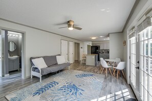 Uma sala de estar moderna com um sofá cinzento, cadeiras brancas, um tapete estampado e um ventilador de teto.