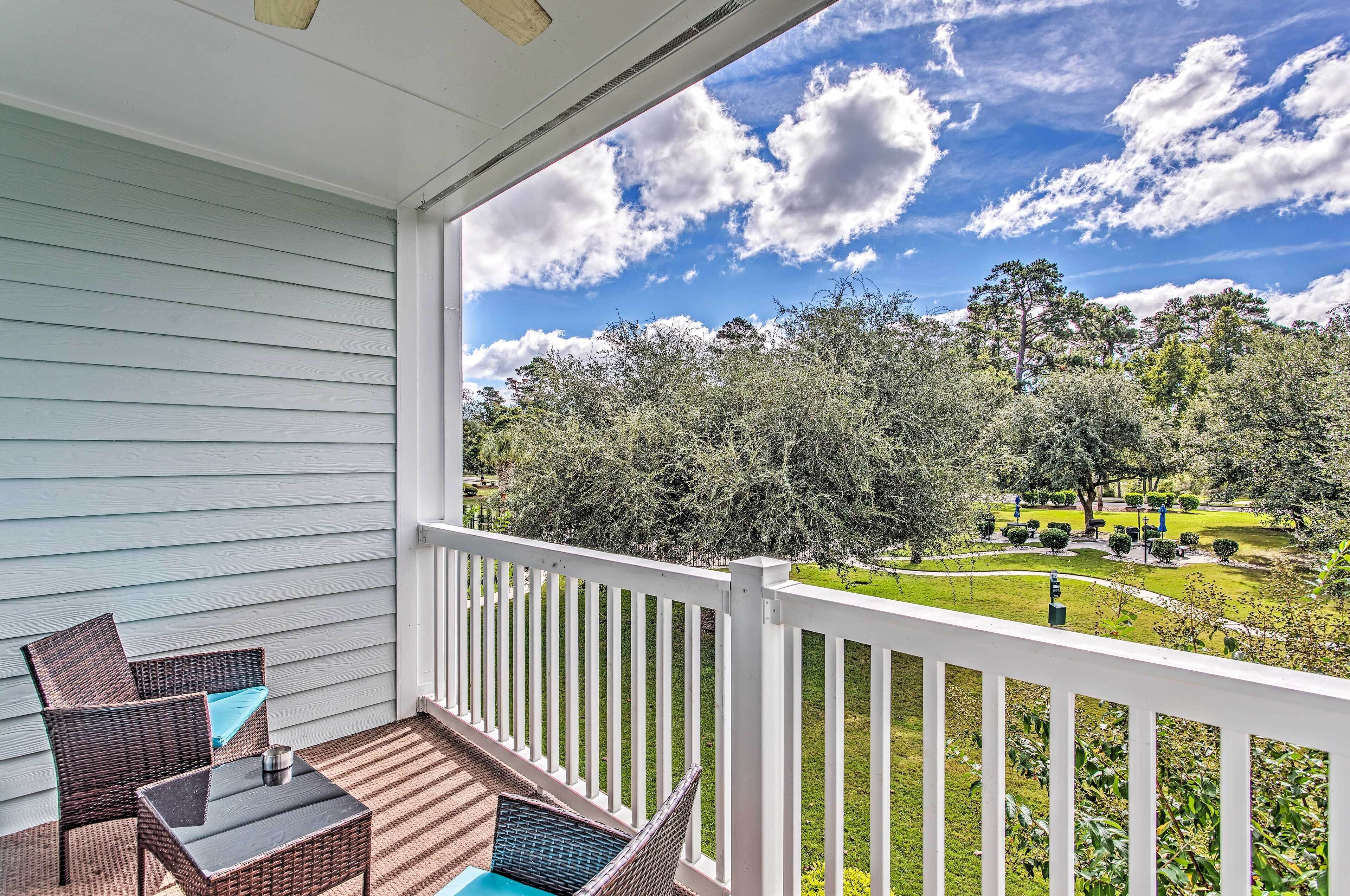 A balcony with wicker furniture and a clear view of a well-maintained garden and trees.