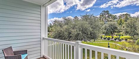 A balcony with wicker furniture and a clear view of a well-maintained garden and trees.