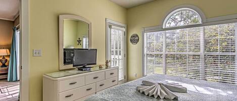 A bedroom with a bed, dresser, television, and large windows with blinds.