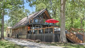 A cabin with a wooden deck, a red umbrella, and a staircase leading to the upper level. - Furnished Deck + Lake Access: Fairland Log Cabin (Fairland)