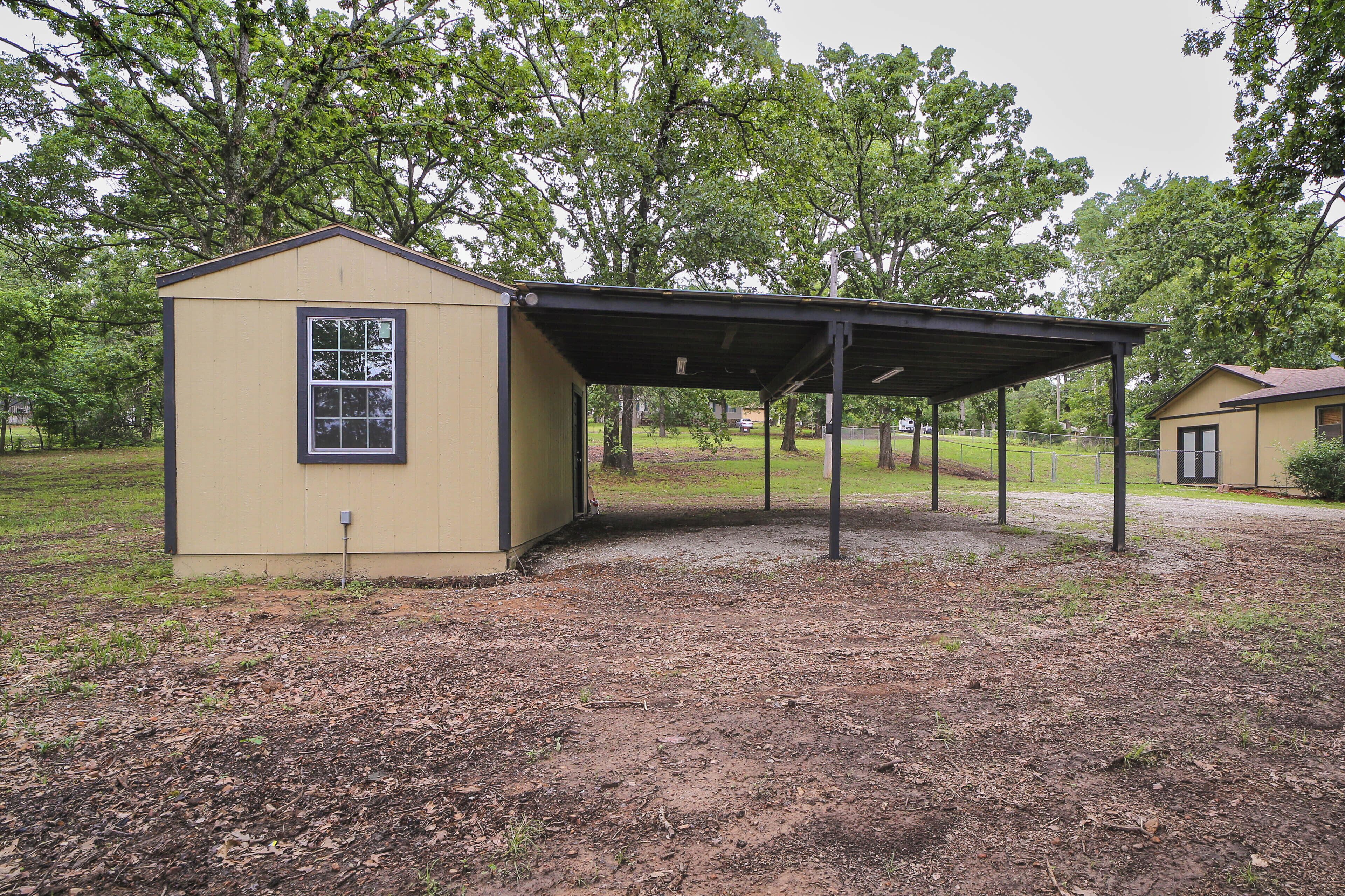 A small, single-story building with a covered outdoor area, surrounded by trees and a grassy field.