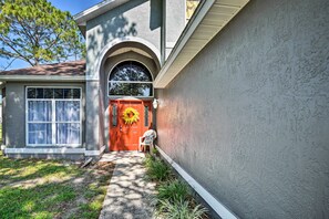 A house with a red door, a white chair outside, and a garden area.