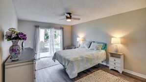 A bedroom with a bed, bedside lamps, a ceiling fan, a window with curtains, and a vase with flowers on a dresser. - 7 Mi to Beach: Pet-friendly Home in Port Orange! (Port Orange)