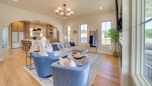 A spacious living room with a large sectional sofa, a dining area with a kitchen in the background, and a large window providing natural light. - Charming Carlton Landing Home: Walk to Lake! (Eufaula)