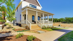 A two-story house with a covered porch, a front yard with landscaping, and a clear blue sky. - Charming Carlton Landing Home: Walk to Lake! (Eufaula)