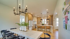 A modern kitchen with a central island, white cabinetry, and a dining area with a large table and chairs. - Charming Carlton Landing Home: Walk to Lake! (Eufaula)