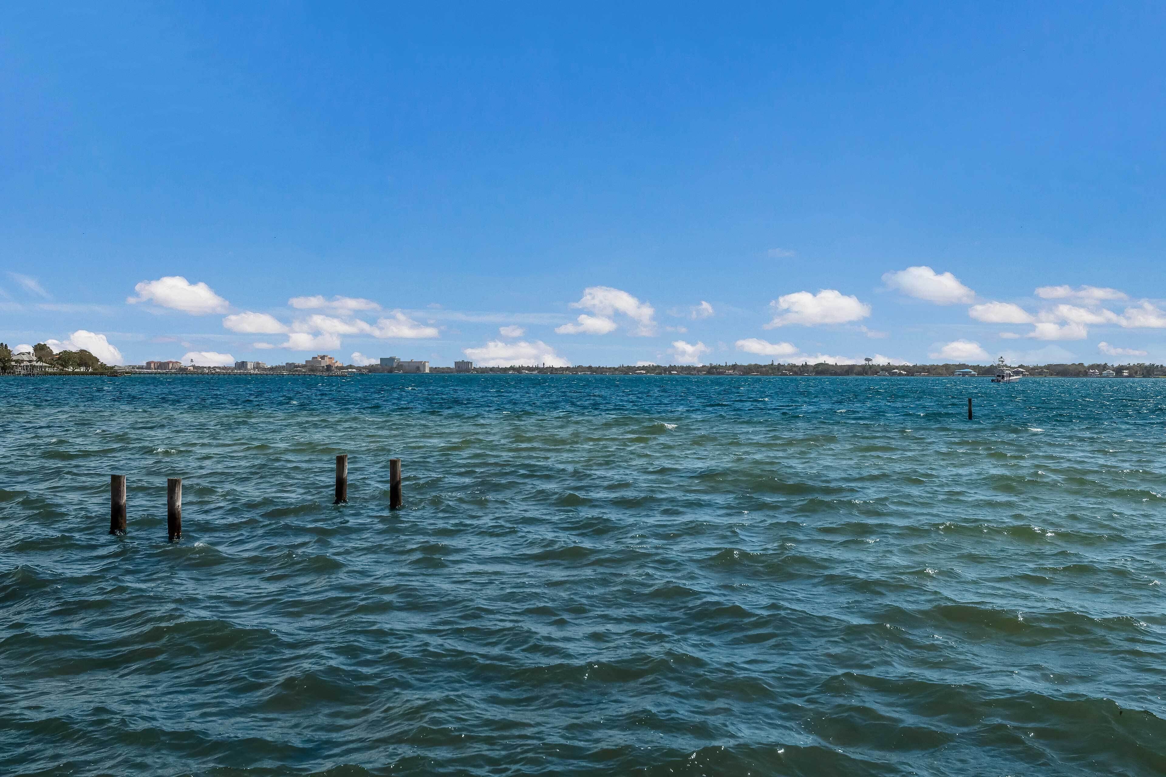 A waterfront view with calm water, a distant shoreline, and a clear sky.