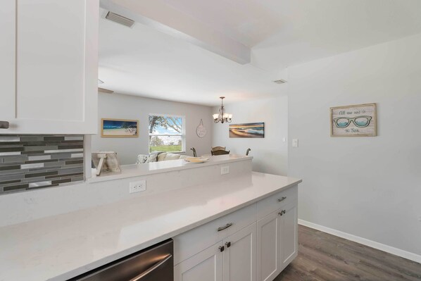 A modern kitchen with white cabinetry, a large island with a sink, and a view of the outdoors through a window.