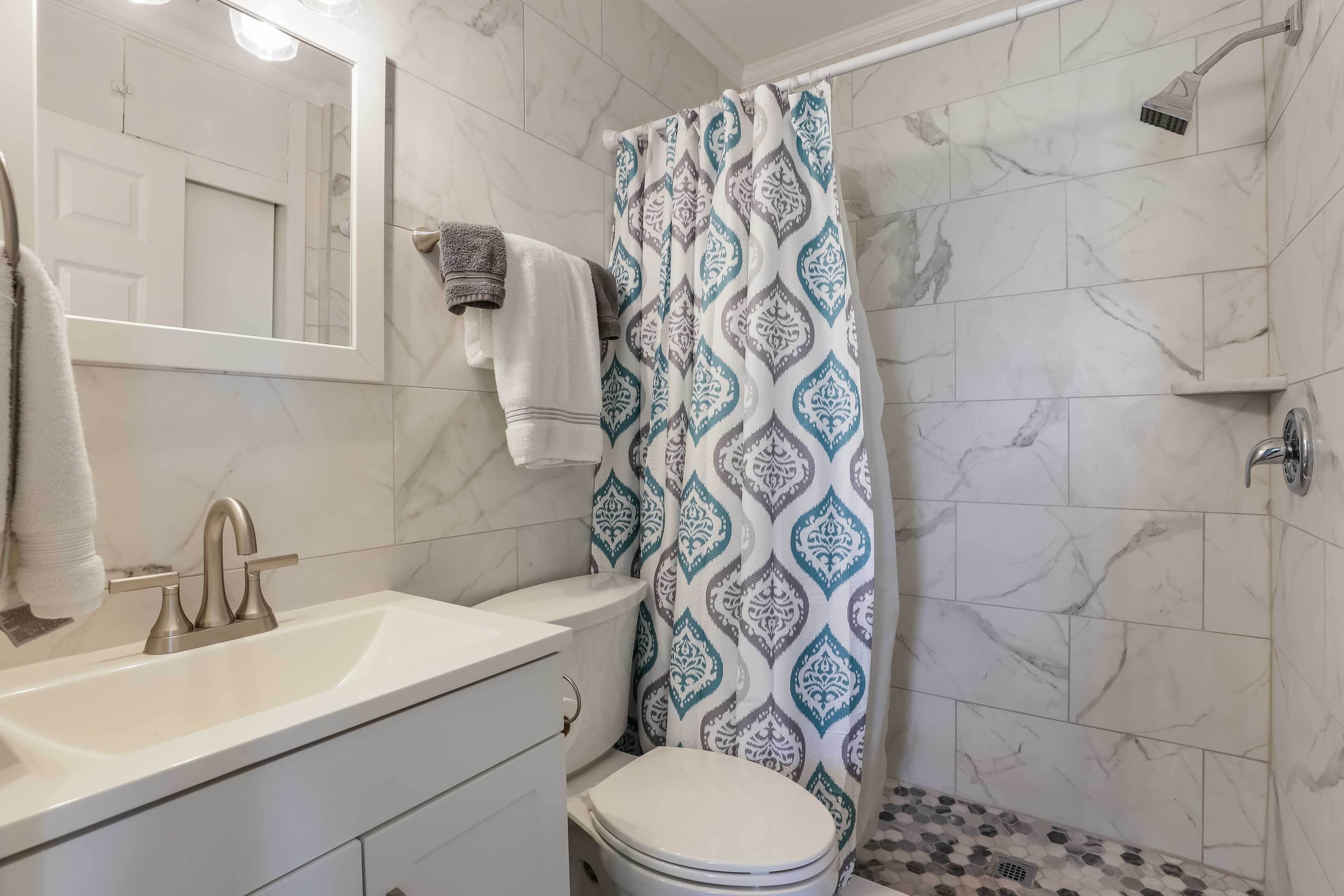 A bathroom with a white sink, a mirror, a toilet, and a shower with a patterned curtain.