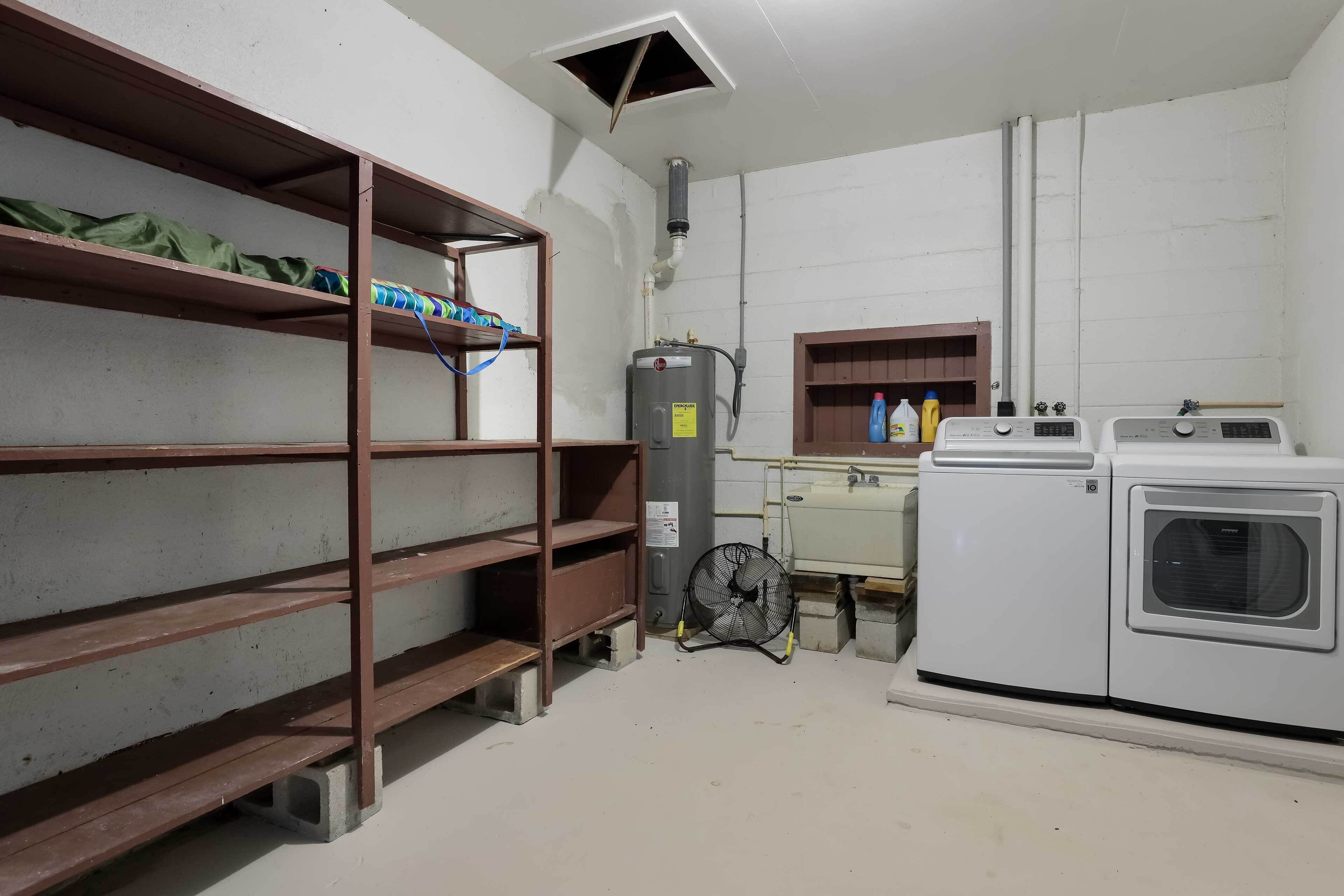 A laundry room with a washing machine, dryer, and shelves with various items.