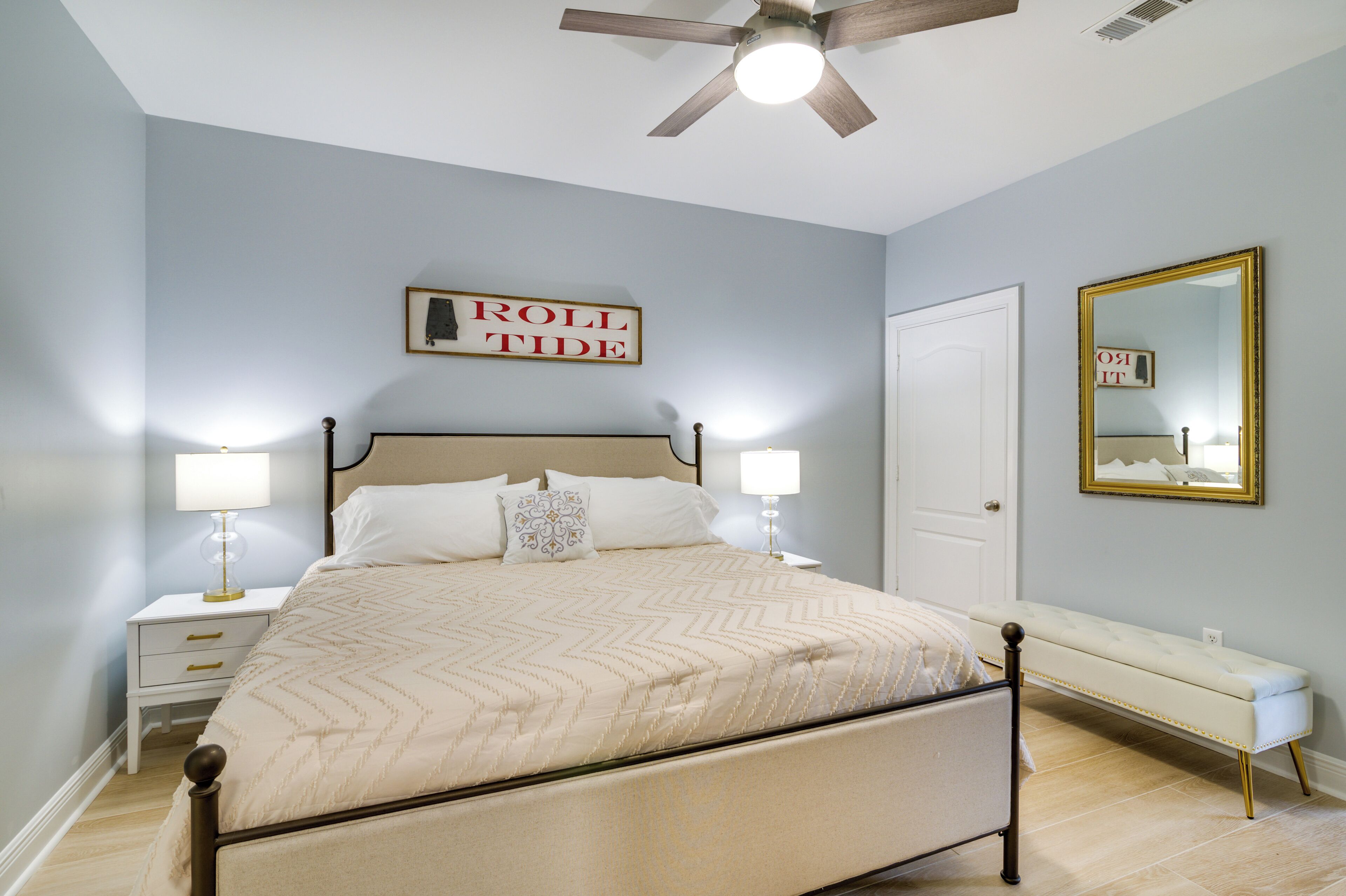 A bedroom with a bed, nightstands, a bench, a ceiling fan, and a mirror.