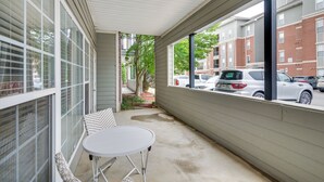 Un espacio exterior cubierto con una mesa y sillas, vista a coches estacionados y un edificio con amplias ventanas al fondo.