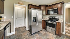 A kitchen with a stainless steel refrigerator, a microwave, and an oven. There is a door with a sign above it, and the floor is tiled.
