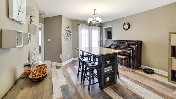 A modern kitchen with a central island, bar stools, a piano, and a chandelier.