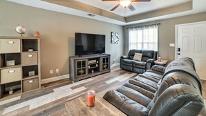 A living room with a leather sofa, a television on a wooden stand, a ceiling fan, and a patterned rug.