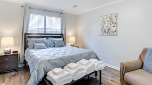 A bedroom with a bed, bedside lamps, a bedside table, a chair, and a wall-mounted artwork. - North Charleston Vacation Rental Near Cooper River (North Charleston)