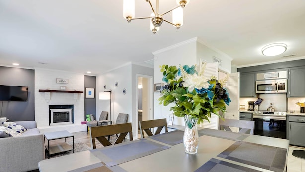 A modern living room with a fireplace, a dining area with a vase of flowers, and a kitchen with grey cabinets and stainless steel appliances. - North Charleston Vacation Rental Near Cooper River (North Charleston)
