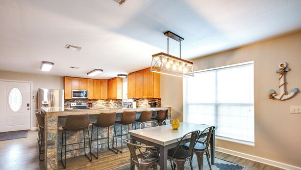 A modern kitchen with a central island, bar stools, and a dining table with chairs. - Point Blank Vacation Rental w/ Large Patio! (Pointblank)