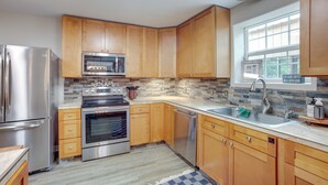 A modern kitchen with wooden cabinets, stainless steel appliances, a built-in oven, and a large window providing natural light. - Point Blank Vacation Rental w/ Large Patio! (Pointblank)