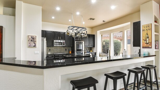 A modern kitchen with black countertops, stainless steel appliances, and a central island with bar stools. - Luxe Couples Retreat w/ Pool & Outdoor Kitchen! (Phoenix)