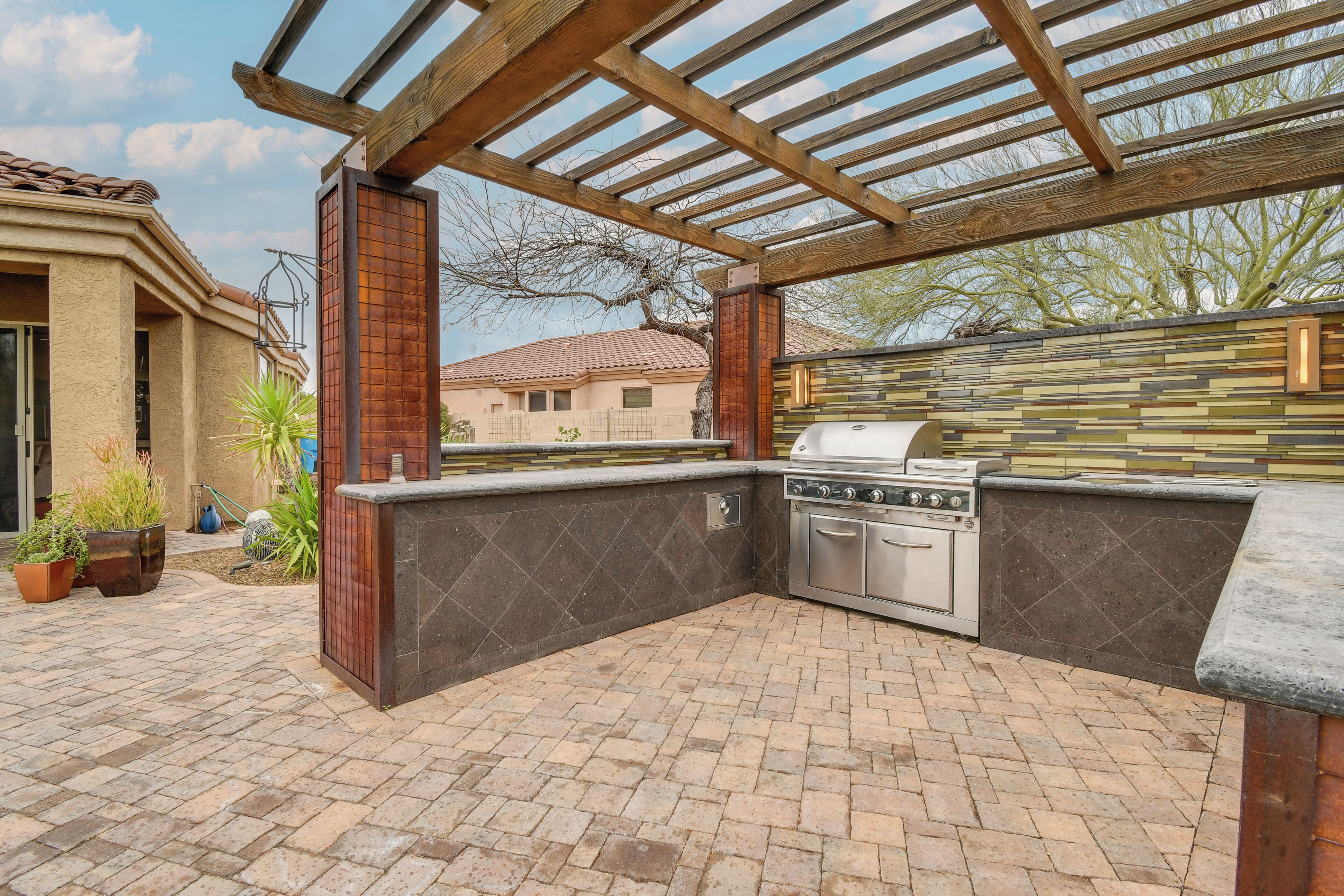 Een buitenkeuken met een grill, ingebouwde oven en een pergola erboven.