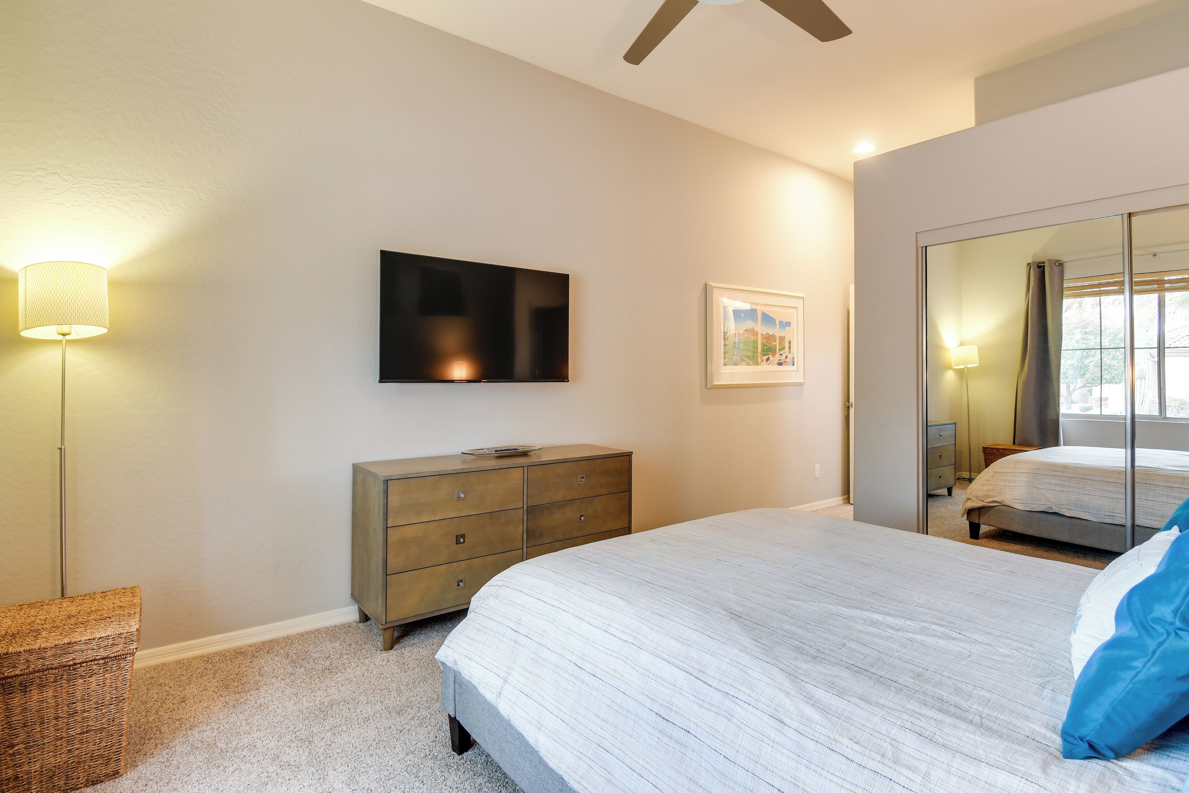 Un dormitorio con cama, cómoda, televisor y un espejo grande.