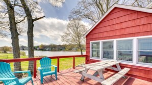 Un terrazzo in legno con tavolo da picnic e due poltrone Adirondack color turchese, con vista su un lago.