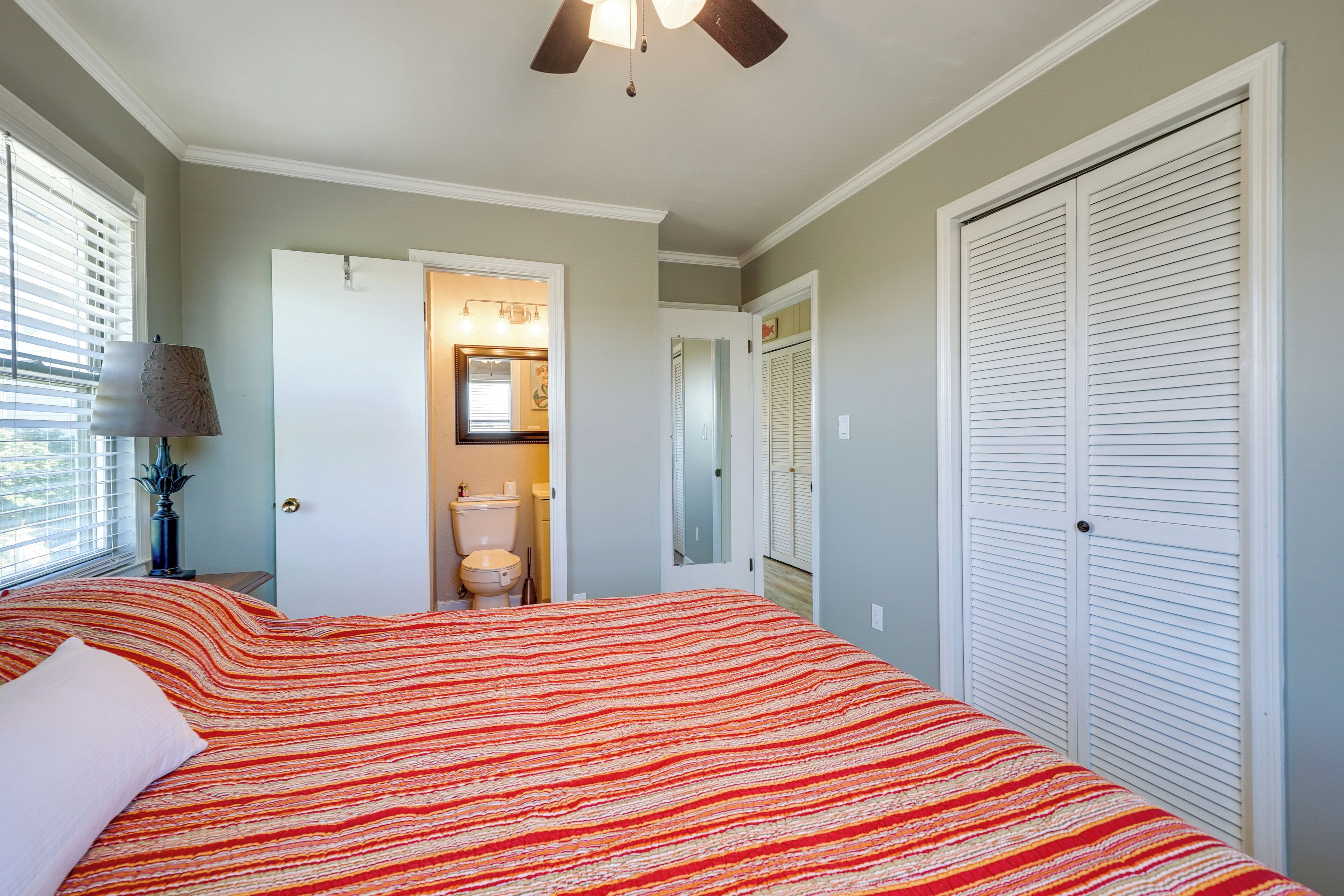 A bedroom with a bed, a ceiling fan, a nightstand with a lamp, and a closet.