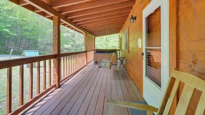 A wooden cabin with a covered porch, a small seating area, and a view of the surrounding forest.
