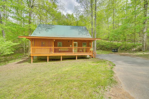 Une cabane en bois avec un toit vert, une véranda et un petit jardin devant.